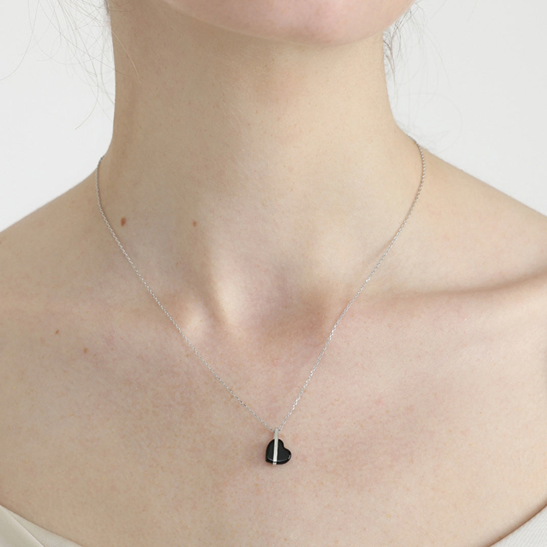 Necklace with a heart-shaped black onyx pendant worn by a person on a white background