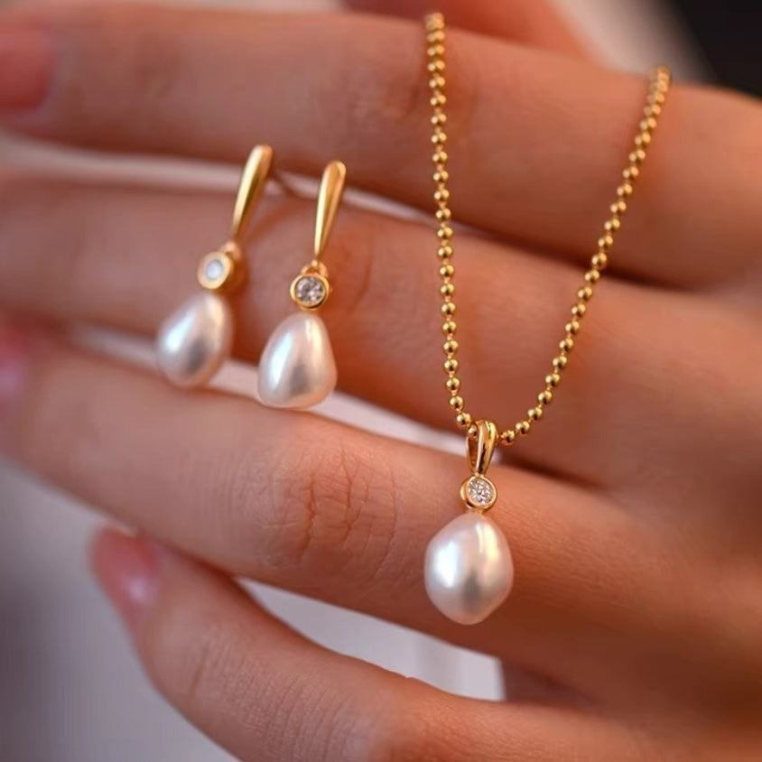 Close-up of a matching bridal jewelry set featuring natural baroque pearl drop earrings and a pendant necklace in 18K gold vermeil held in hand.