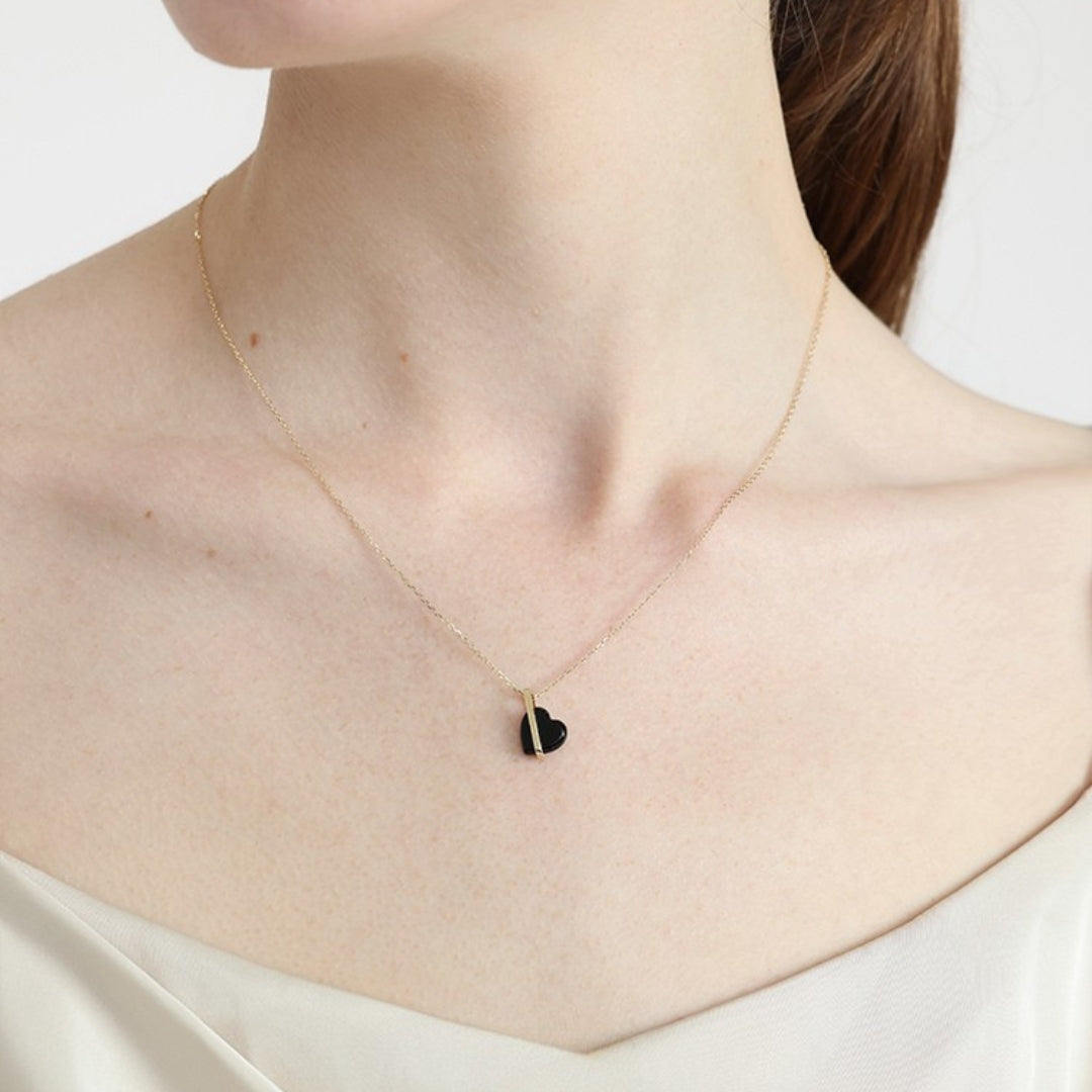 Necklace with a black heart pendant worn by a person on a white background