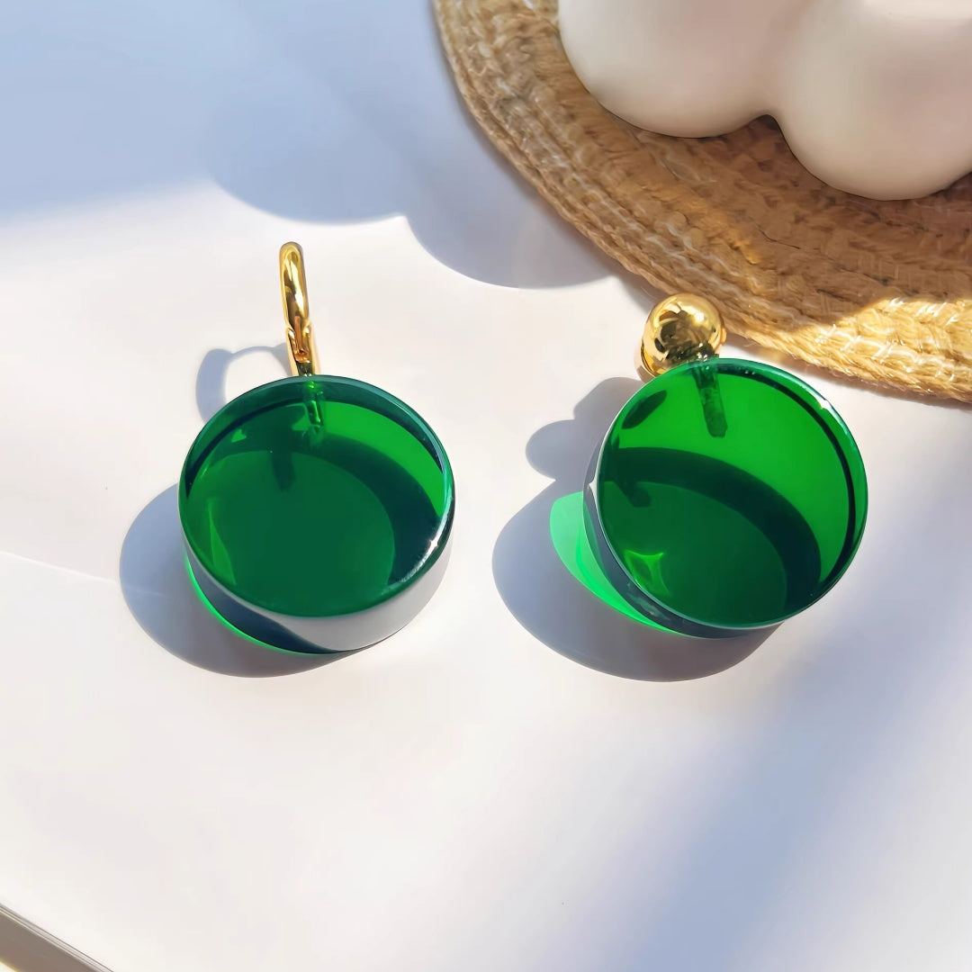 A pair of emerald green translucent glass earrings with 18K gold-plated brass accents reflecting natural sunlight.