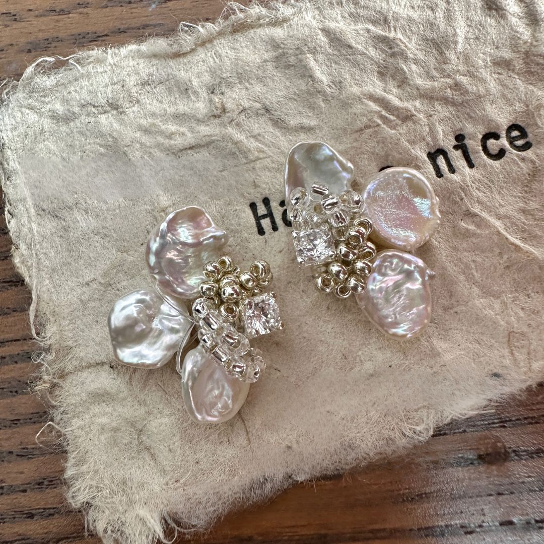 A pair of handmade statement wedding flower earrings with delicate floral designs, adorned with white pearl accents and a central baroque pearl drop, showcasing the beauty of freshwater pearl jewelry. These luxury handmade statement pearl earrings are ideal as bridal earrings pearl or elegant modern pearl earrings for any occasion.