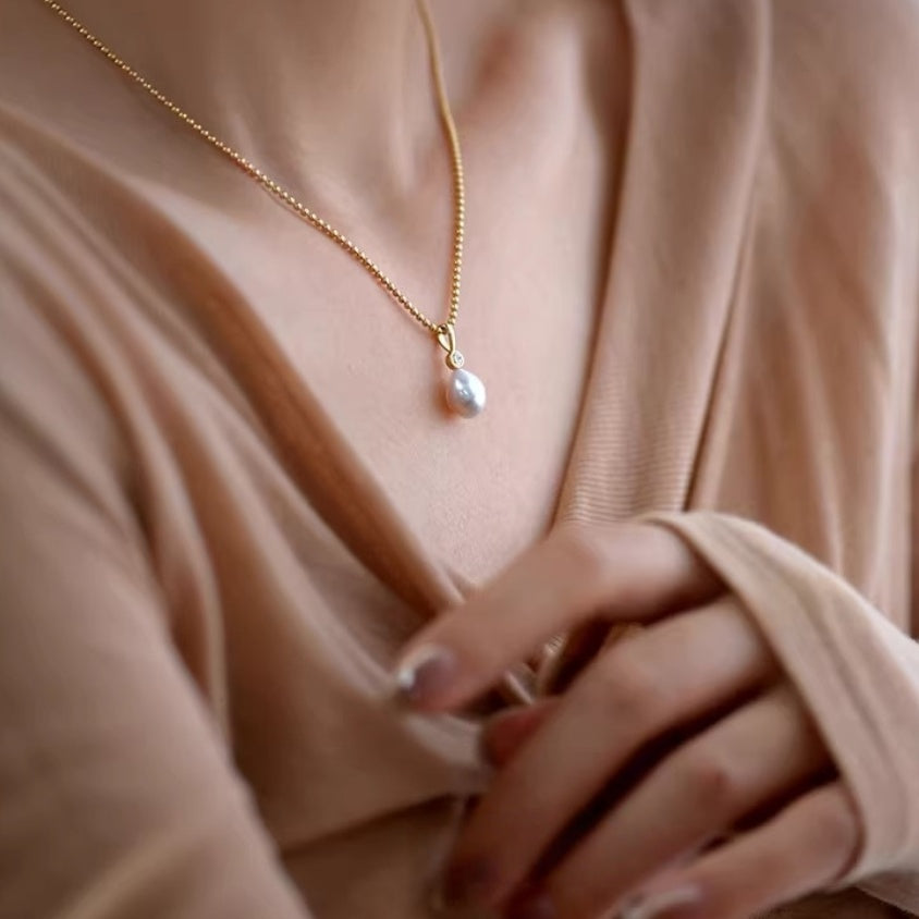 Detail shot of lustrous white teardrop pearl pendants hanging from delicate gold ball chains, showing the organic baroque shape. 5