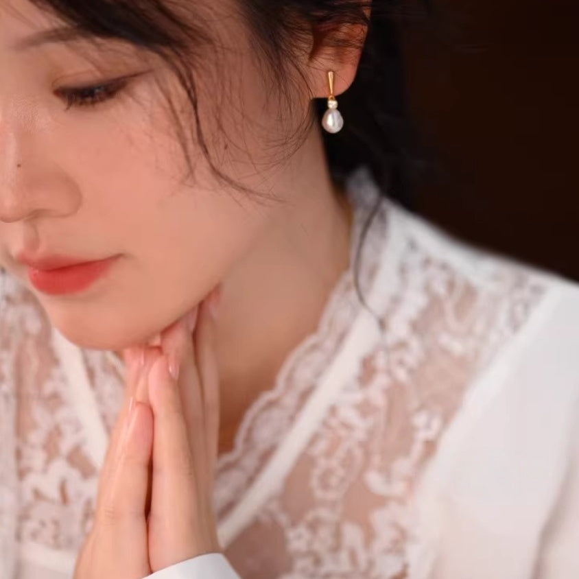 Bride wearing pearl drop earrings and a white lace dress with hands clasped, capturing a romantic wedding moment. 1