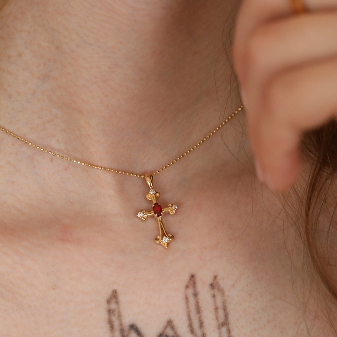 Gold necklace with a cross pendant featuring a ruby gemstone and diamond on a person's neck.