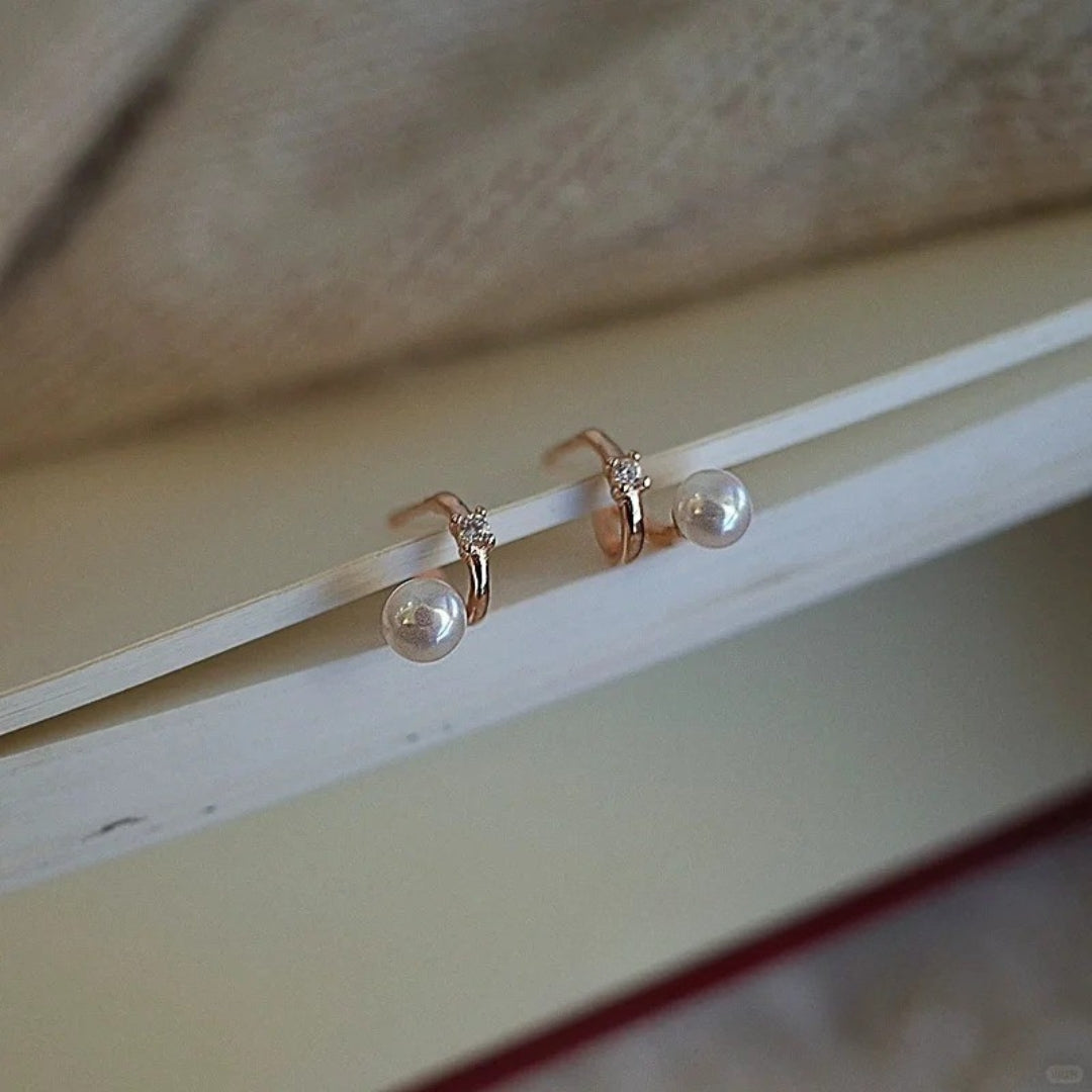 Pair of gold diamond huggie earrings on a light wooden surface