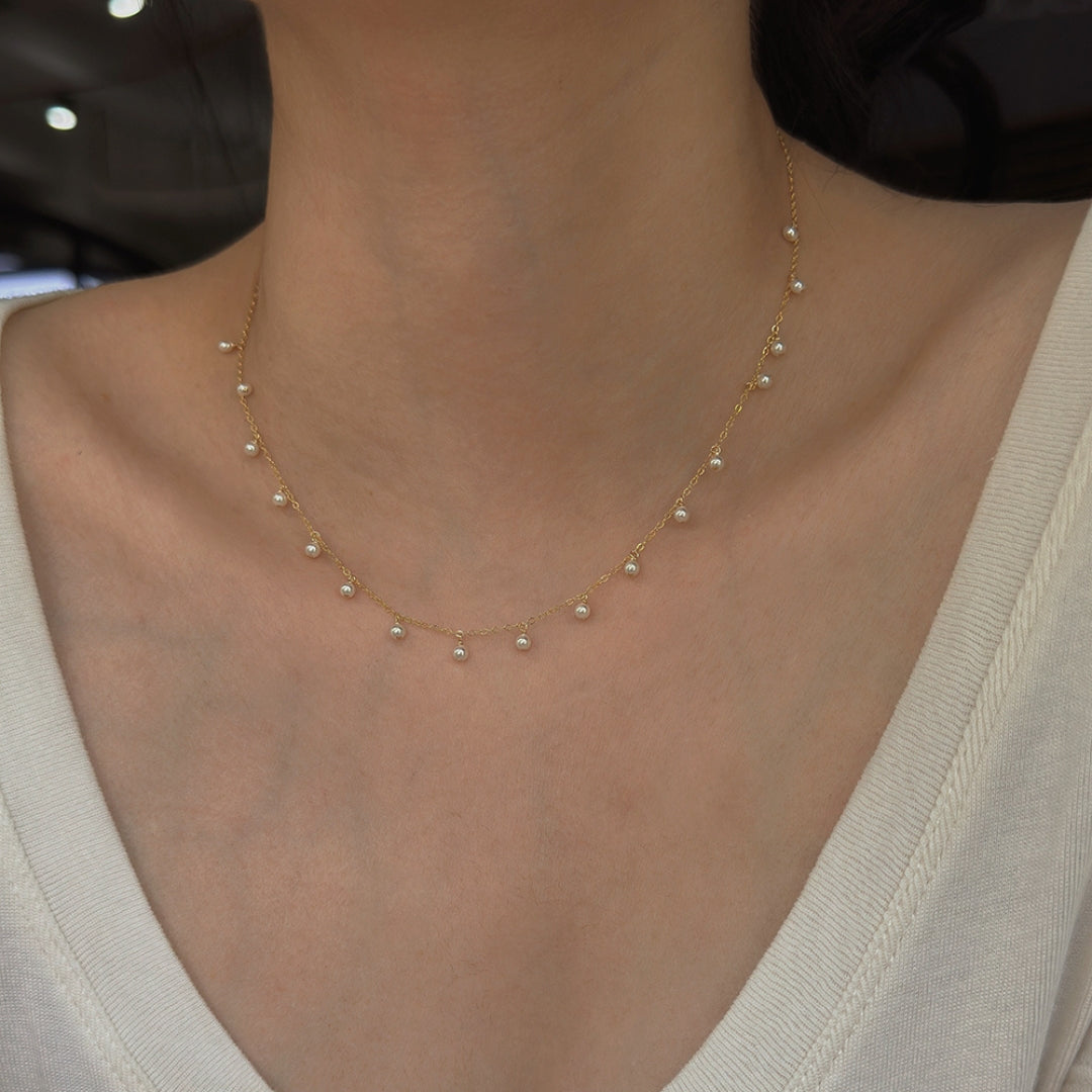 A dainty pearl necklace choker on a person wearing a beige top.