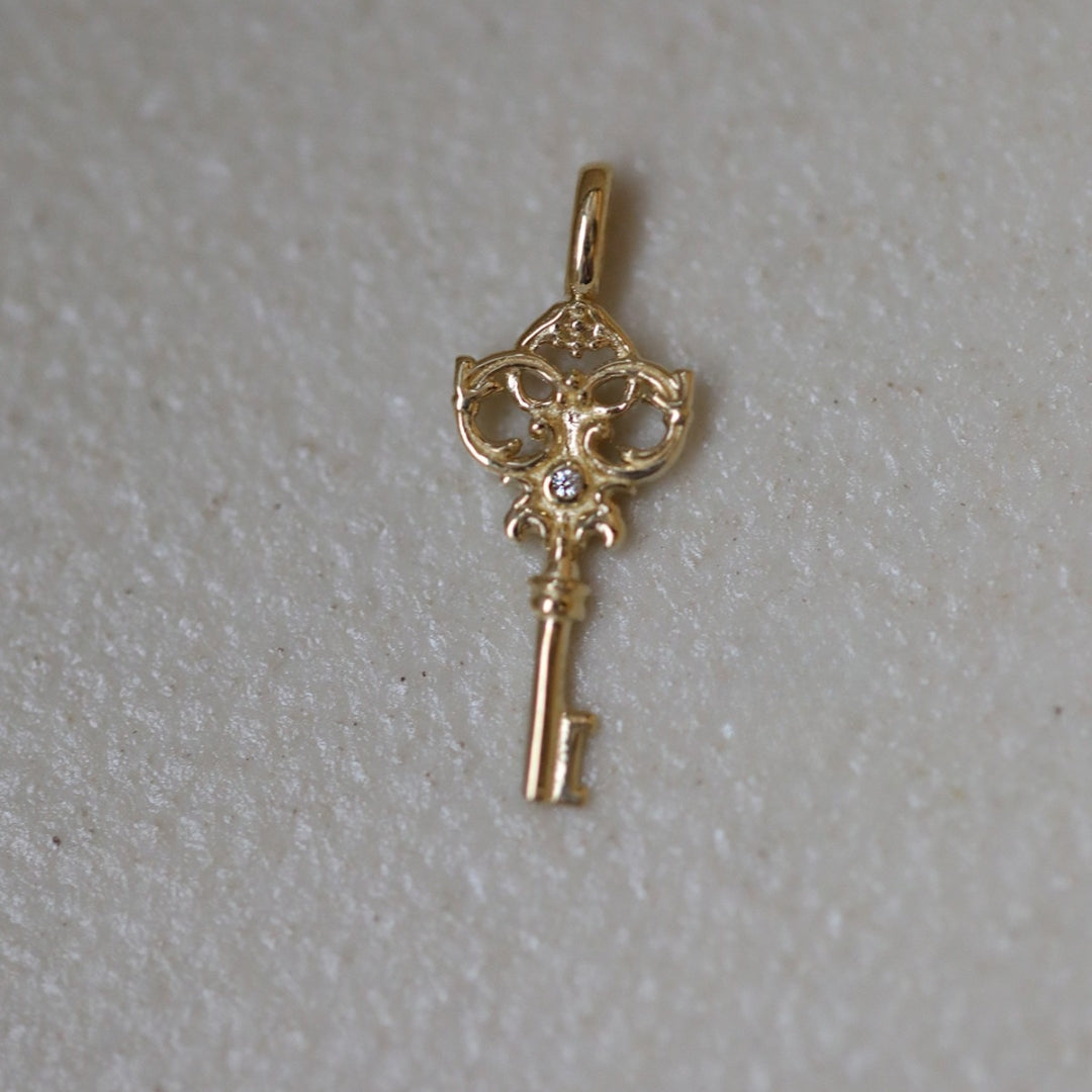 9k Gold key pendant centered with a sparkling diamond on a light gray background