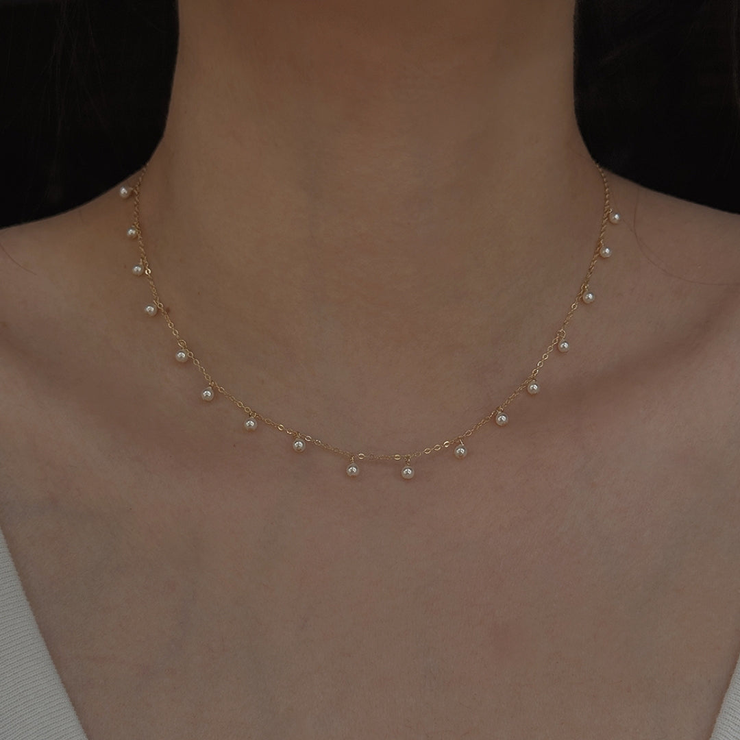Delicate gold and pearl necklace on a person's neck against a dark background