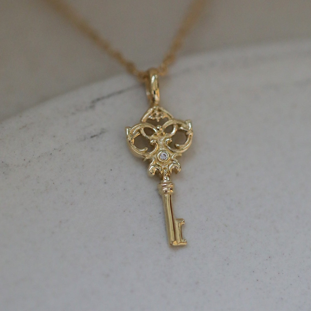 Gold key pendant necklace against a marble background