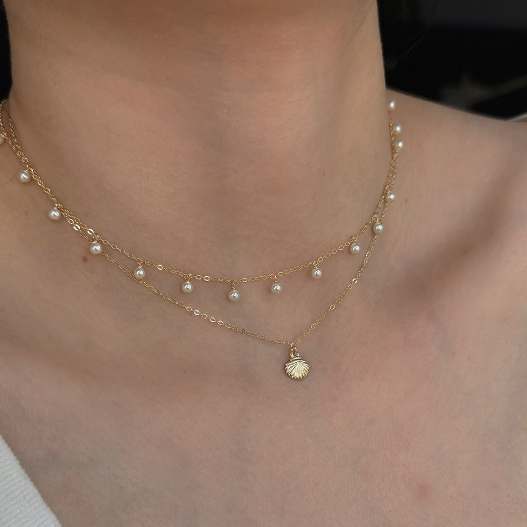 A layered pearl necklace and a shell pendant necklace on a person's neck.