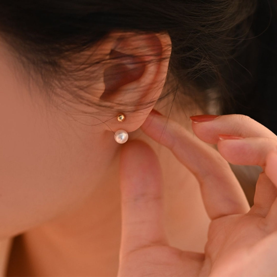 Close-up of a person wearing a pair of gold pearl earrings with a blurred background.