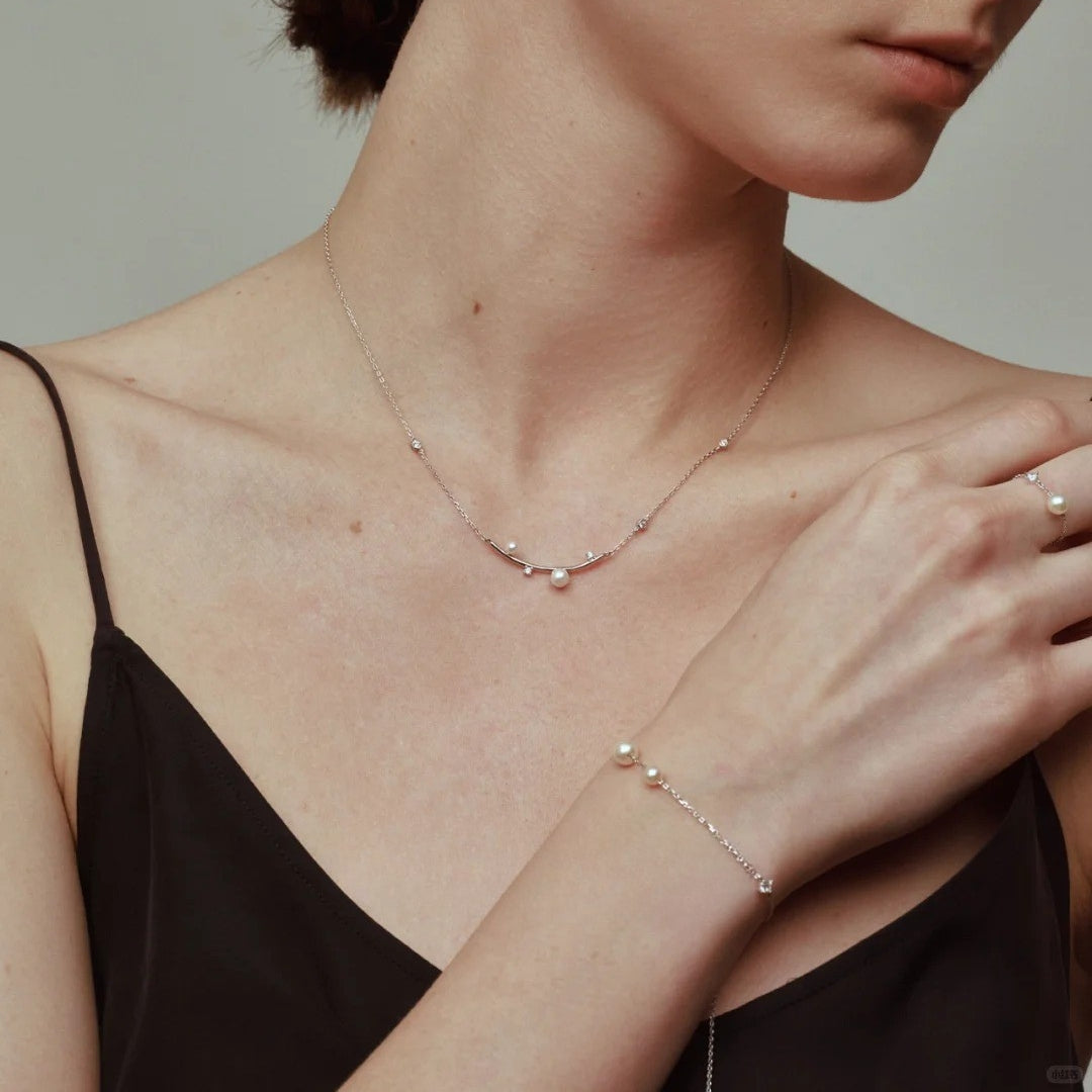 Woman wearing a delicate pearl diamond necklace and diamond pearl bracelet on a neutral background