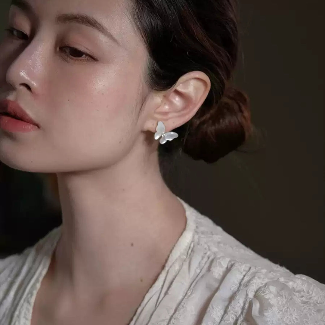 Close-up of a woman wearing butterfly earrings with a neutral background