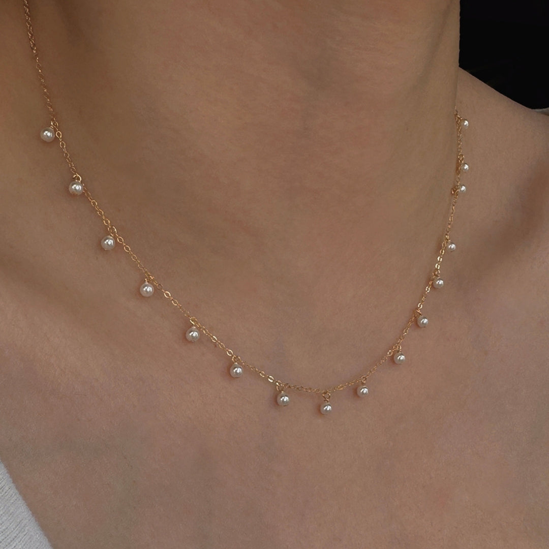 Dainty pearl necklace choker on a person's neck against a neutral background.