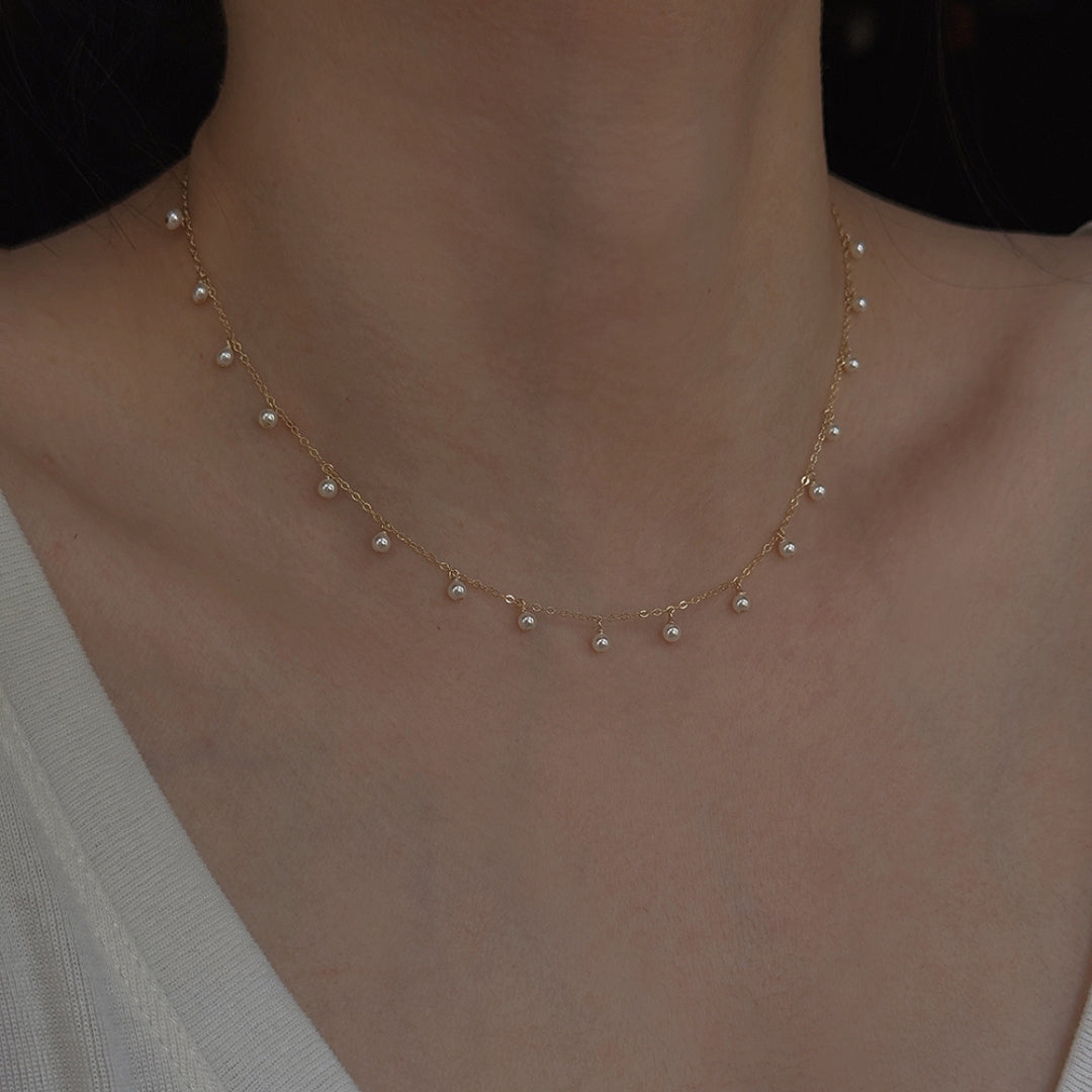 Gold pearl necklace on a person's neck against a dark background