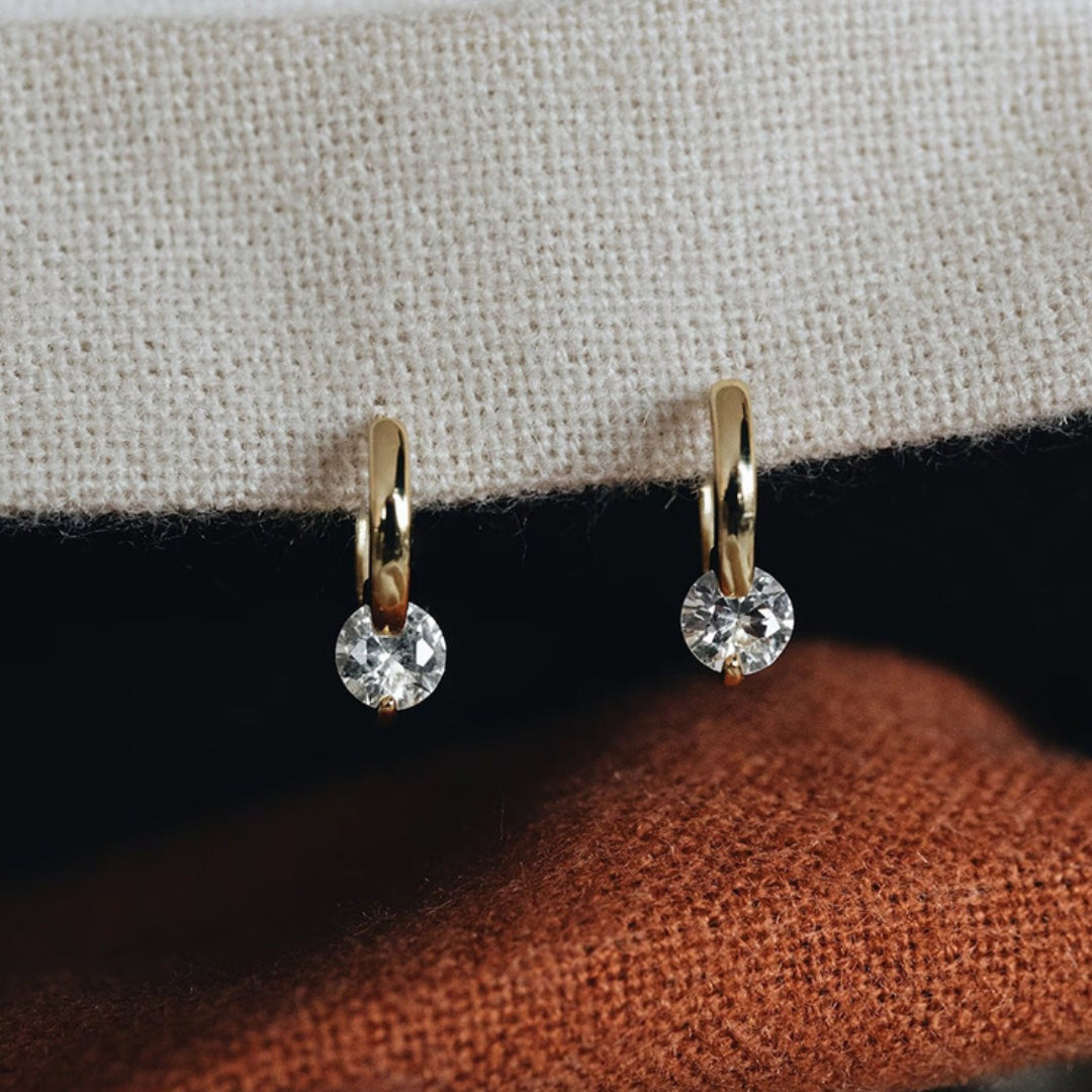 A pair of 14K gold hoop earrings with diamond on a textured surface
