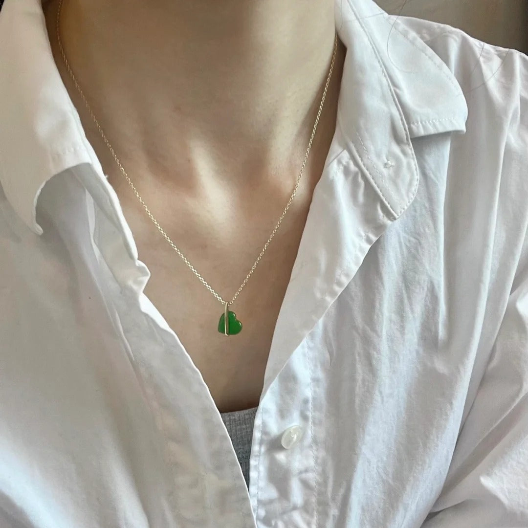 Green heart-shaped pendant with gold necklace on a white shirt