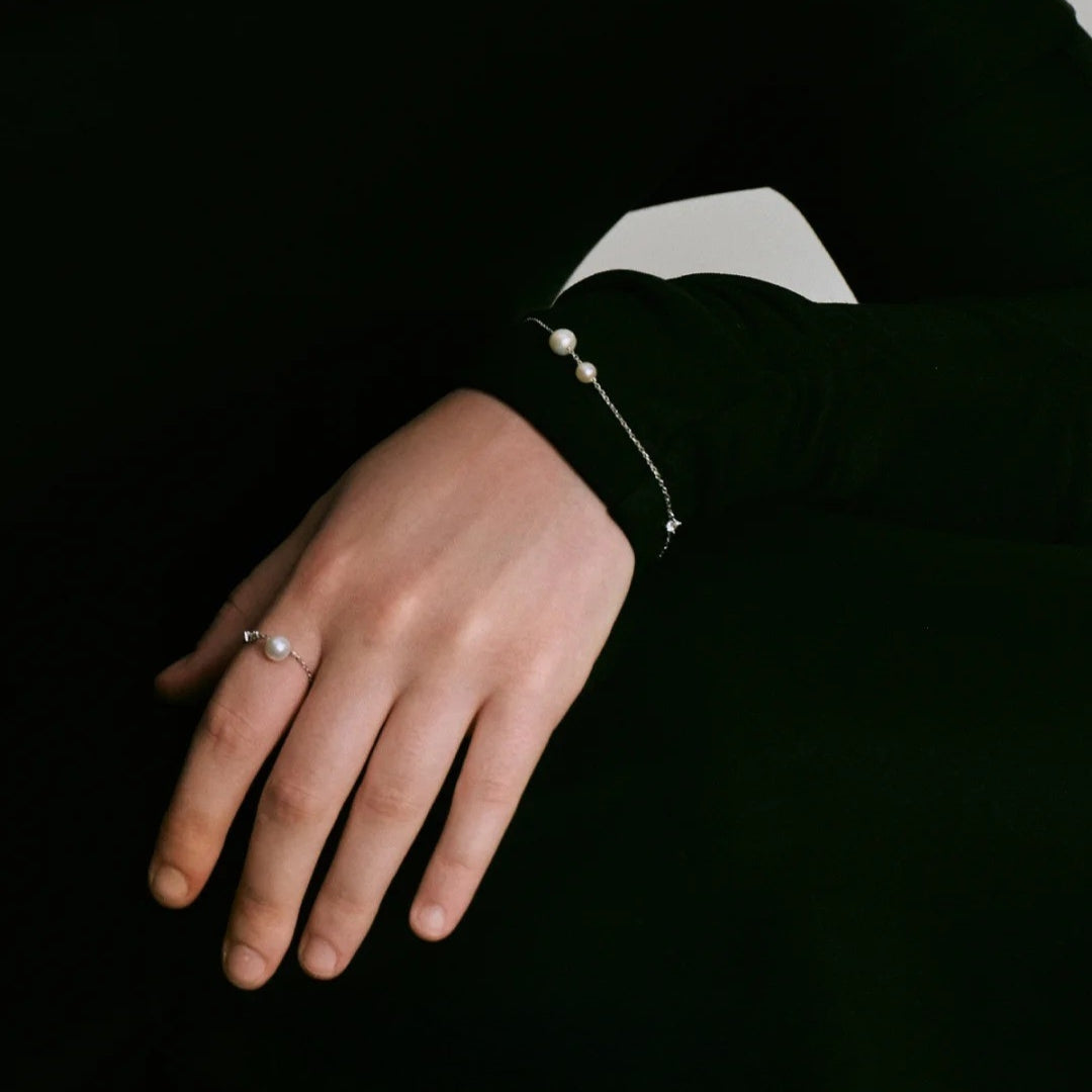 Hand wearing a pearl bracelet and silver pearl ring with a black background