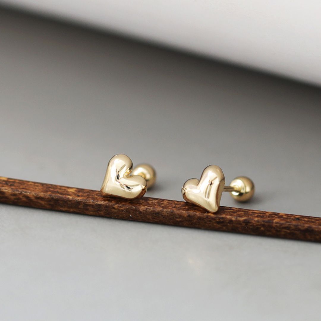 A pair of tiny gold heart studs with a delicate, minimalist design. These gold heart stud earrings showcase a classic Korean jewelry style, perfect for everyday wear.