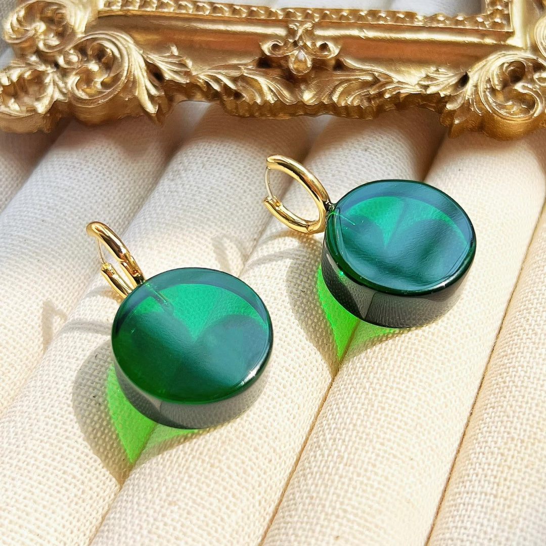 Elegant round green glass earrings displayed next to a gold vintage frame, highlighting a retro aesthetic.