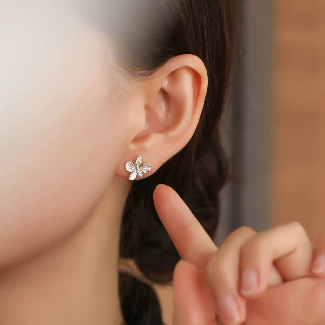 Close-up of an ear wearing a silver iris flower earring with a blurred background