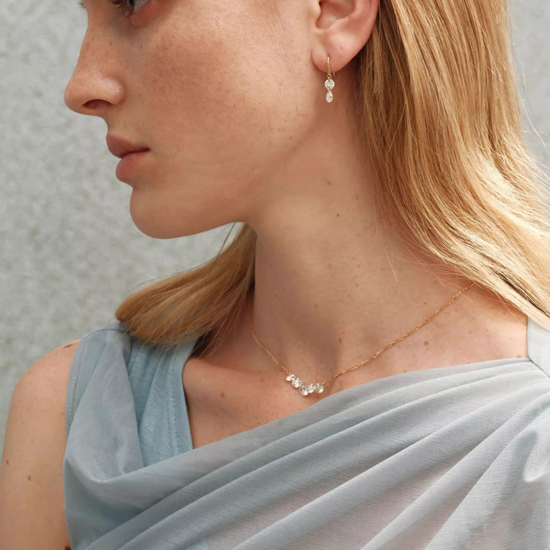 Close up of a model wearing moissanite smile necklace and drop earrings highlighting the light-reflecting fire of the stones.